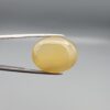 Multi-angle macro photographs of a 26.29-carat natural yellow chalcedony agate (Zard Aqeeq) oval cabochon from Iran held in metal tweezers, showcasing a smooth, domed profile, uniform honey-yellow translucency, and a high-gloss reflective surface.