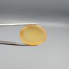 Multi-angle macro photographs of a 26.29-carat natural yellow chalcedony agate (Zard Aqeeq) oval cabochon from Iran held in metal tweezers, showcasing a smooth, domed profile, uniform honey-yellow translucency, and a high-gloss reflective surface.