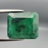 Macro photograph of a 6.46-carat natural emerald (Panna / Zamrud) from the Swat Valley in Pakistan held in metal tweezers, showcasing an emerald cut, a rich green body, and distinctive natural dark mineral dispersions across the stone.
