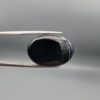 Multi-angle macro photographs of a 26.33-carat natural black banded agate (Sulemani Aqeeq) oval cabochon held in metal tweezers, showcasing a mirror-polished obsidian black surface accented with three distinct, parallel curving white stripes across its face.