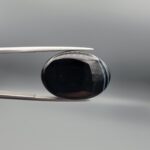 Multi-angle macro photographs of a 26.33-carat natural black banded agate (Sulemani Aqeeq) oval cabochon held in metal tweezers, showcasing a mirror-polished obsidian black surface accented with three distinct, parallel curving white stripes across its face.