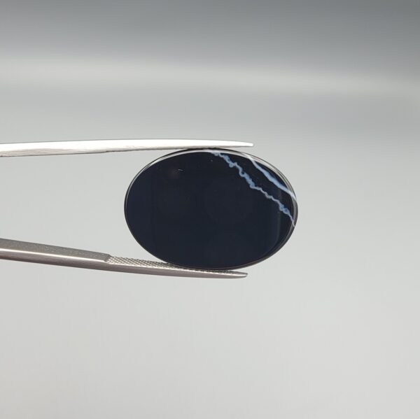 Multi-angle macro photographs of a 26.88-carat natural black banded agate (Sulemani Aqeeq) oval cabochon held in metal tweezers, showcasing a high-gloss obsidian black dome with an intricate, wavy organic white veining pattern across the surface.