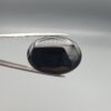Multi-angle macro photographs of a 26.96-carat natural black banded agate (Sulemani Aqeeq) oval cabochon held in metal tweezers and fingertips, showcasing a mirror-polished obsidian black surface with sharp, angular chevron-style white banding lines across the face.