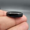 Multi-angle macro photographs of a 27.51-carat natural black banded agate (Sulemani Aqeeq) oval cabochon held in metal tweezers and fingertips, showcasing a mirror-polished deep obsidian black surface accented by fine, undulating white banding lines traversing across the polished surface.
