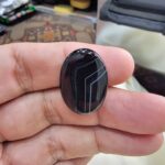 Remarkable 24.94 carat natural black banded agate (Sulemani Aqeeq), expertly finished into a high-gloss oval cabochon featuring architecturally crisp white angular geometry and fine parallel fortification lines across a jet-black body.