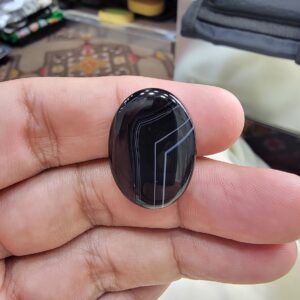Remarkable 24.94 carat natural black banded agate (Sulemani Aqeeq), expertly finished into a high-gloss oval cabochon featuring architecturally crisp white angular geometry and fine parallel fortification lines across a jet-black body.