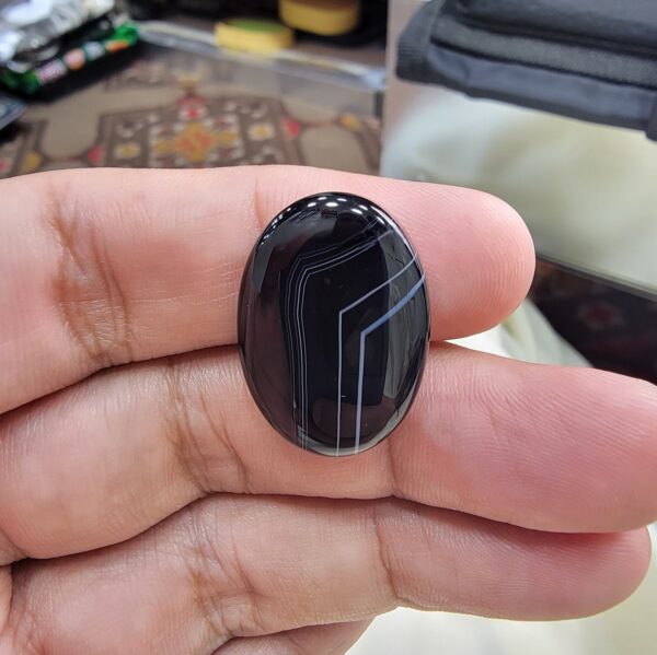 Remarkable 24.94 carat natural black banded agate (Sulemani Aqeeq), expertly finished into a high-gloss oval cabochon featuring architecturally crisp white angular geometry and fine parallel fortification lines across a jet-black body.