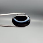 Exceptional 26.53 carat natural black banded agate (Sulemani Aqeeq), expertly finished into a high-gloss oval cabochon displaying a bold, curved concentric white band wrapping seamlessly around an intense jet-black core.