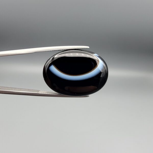 Exceptional 26.53 carat natural black banded agate (Sulemani Aqeeq), expertly finished into a high-gloss oval cabochon displaying a bold, curved concentric white band wrapping seamlessly around an intense jet-black core.