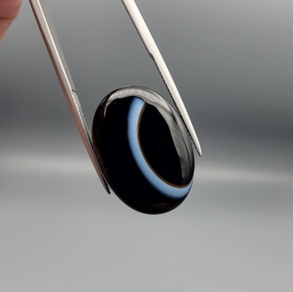 Exceptional 26.53 carat natural black banded agate (Sulemani Aqeeq), expertly finished into a high-gloss oval cabochon displaying a bold, curved concentric white band wrapping seamlessly around an intense jet-black core.