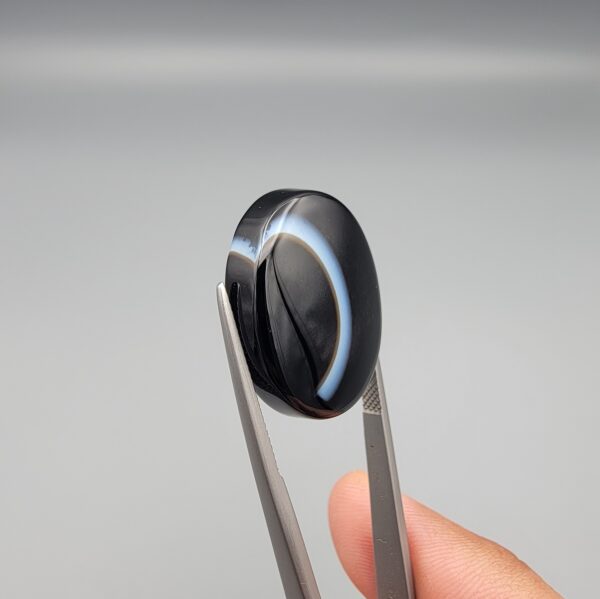 Exceptional 26.53 carat natural black banded agate (Sulemani Aqeeq), expertly finished into a high-gloss oval cabochon displaying a bold, curved concentric white band wrapping seamlessly around an intense jet-black core.