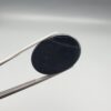 Multi-angle macro photographs of a 24.97-carat natural black banded agate (Sulemani Aqeeq) oval cabochon held in metal tweezers, displaying a mirror-polished deep obsidian black surface accented by crisp, fine diagonal white banding lines running across the face.