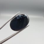 Rare 25.51 carat natural black banded agate (Sulemani Aqeeq) featuring a high-gloss finish and a captivating, crown-like cluster of orbicular cellular white eye formations along the top border of a jet-black cabochon.