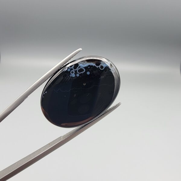Rare 25.51 carat natural black banded agate (Sulemani Aqeeq) featuring a high-gloss finish and a captivating, crown-like cluster of orbicular cellular white eye formations along the top border of a jet-black cabochon.
