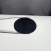 Multi-angle macro photographs of a 27.16-carat natural black banded agate (Sulemani Aqeeq) oval cabochon held in metal tweezers, showcasing an intense mirror-polished deep obsidian black surface accented by a meandering white scalloped or lace-like banding arc across the face.