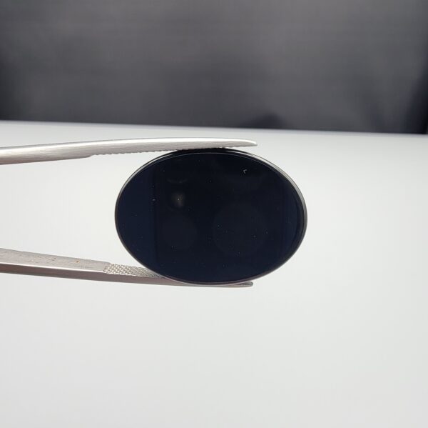 Multi-angle macro photographs of a 27.16-carat natural black banded agate (Sulemani Aqeeq) oval cabochon held in metal tweezers, showcasing an intense mirror-polished deep obsidian black surface accented by a meandering white scalloped or lace-like banding arc across the face.