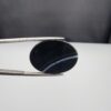 Multi-angle macro photographs of a 26.14-carat natural black banded agate (Sulemani Aqeeq) oval cabochon held in metal tweezers, showcasing a mirror-polished deep obsidian black dome with prominent, gently curved white banding lines traversing across the polished surface.