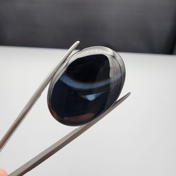 Rare 26.66 carat natural black banded agate (Sulemani Aqeeq) featuring a mirror-polished deep black body traversed by an extraordinary, luminous blue-gray and bright white eye-like arc.