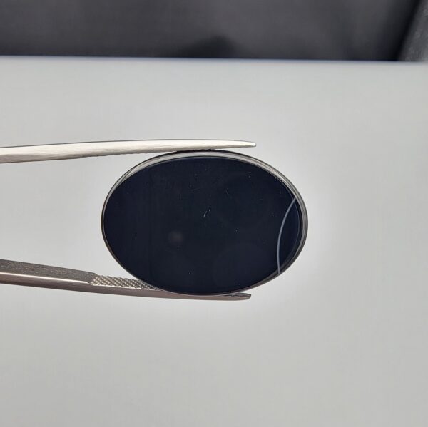 Multi-angle macro photographs of a 26.84-carat natural black banded agate (Sulemani Aqeeq) oval cabochon held in metal tweezers, showcasing a mirror-polished deep obsidian black surface accented by a single, distinct curved white banding line along the right edge.