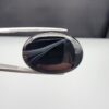Multi-angle macro photographs of a 25.17-carat natural black banded agate (Sulemani Aqeeq) oval cabochon held in metal tweezers, showcasing a mirror-polished deep obsidian black surface accented by multiple fine, sharp parallel white banding lines sweeping diagonally across the face.