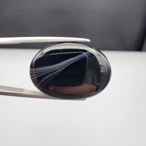 Multi-angle macro photographs of a 25.17-carat natural black banded agate (Sulemani Aqeeq) oval cabochon held in metal tweezers, showcasing a mirror-polished deep obsidian black surface accented by multiple fine, sharp parallel white banding lines sweeping diagonally across the face.