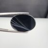 Multi-angle macro photographs of a 25.17-carat natural black banded agate (Sulemani Aqeeq) oval cabochon held in metal tweezers, showcasing a mirror-polished deep obsidian black surface accented by multiple fine, sharp parallel white banding lines sweeping diagonally across the face.