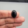 Multi-angle macro photographs of a 10.41-carat natural black banded agate (Sulemani Aqeeq) oval cabochon held on fingertips, showcasing a mirror-polished obsidian black surface contrasting with a wide, sweeping curved band of luminous blue-grey and white forming a bold eye-like pattern.