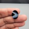 Multi-angle macro photographs of a 10.41-carat natural black banded agate (Sulemani Aqeeq) oval cabochon held on fingertips, showcasing a mirror-polished obsidian black surface contrasting with a wide, sweeping curved band of luminous blue-grey and white forming a bold eye-like pattern.