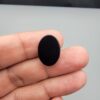 Multi-angle macro photographs of a 9.91-carat natural black banded agate (Sulemani Aqeeq) oval cabochon held on fingertips, displaying a mirror-polished deep obsidian black dome featuring a distinct dual "eye" pattern composed of concentric blue-grey and white rings around dark centers at one end.
