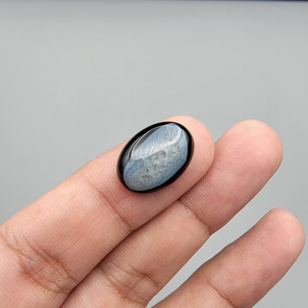 Rare 9.70 carat natural black banded agate (Sulemani Aqeeq), expertly finished into a high-gloss oval cabochon displaying a rich black rim encapsulating a translucent, luminous blue-grey crystalline matrix center.