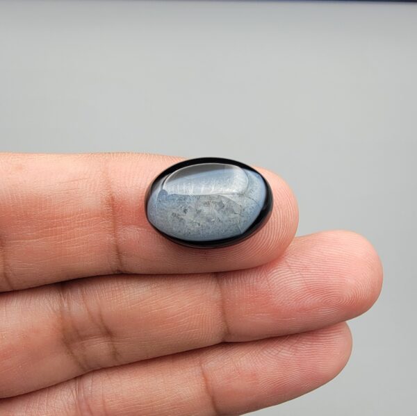 Rare 9.70 carat natural black banded agate (Sulemani Aqeeq), expertly finished into a high-gloss oval cabochon displaying a rich black rim encapsulating a translucent, luminous blue-grey crystalline matrix center.
