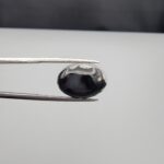 Multi-angle macro photographs of a 9.02-carat natural black banded agate (Sulemani Aqeeq) oval cabochon held in metal tweezers, showcasing a mirror-polished surface featuring an intricate, dense network of black and white crystalline dendritic and mosaic-like fracture patterns across the face.