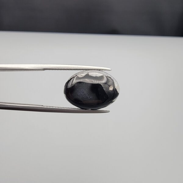 Multi-angle macro photographs of a 9.02-carat natural black banded agate (Sulemani Aqeeq) oval cabochon held in metal tweezers, showcasing a mirror-polished surface featuring an intricate, dense network of black and white crystalline dendritic and mosaic-like fracture patterns across the face.