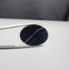 Multi-angle macro photographs of a 15.74-carat natural black banded agate (Sulemani Aqeeq) oval cabochon held in metal tweezers, showcasing a mirror-polished deep obsidian black surface accented by clean, parallel diagonal white banding lines running across the face.