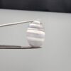 Multi-angle macro photographs of an 18.37-carat natural banded agate (Sulemani Aqeeq) oval cabochon held in metal tweezers, showcasing a smooth, high-gloss surface, translucent monochrome grey-and-white horizontal banding, and fine natural mineral strata.