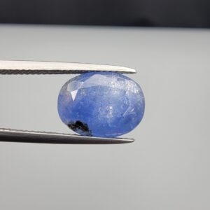 Multi-angle macro photographs of a 7.07-carat natural blue sapphire (Neelam) oval gemstone from Sri Lanka held in metal tweezers, showcasing precision oval faceting, a cornflower blue body, natural internal texturing, and dark mineral inclusions.