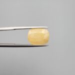 Macro photograph of an 8.45-carat natural yellow sapphire (Pukhraj) cushion-cut gemstone from Sri Lanka held in metal tweezers, showcasing precision faceting, a warm lemon-golden hue, and authentic unheated clarity.