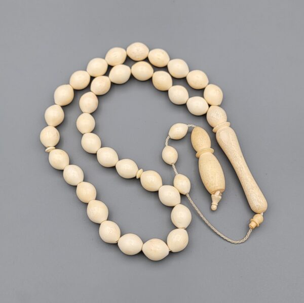 High-resolution macro photograph of a 63.47-gram handmade natural camel bone 33-bead Islamic Tasbih (prayer beads) laid out on a neutral studio backdrop, showcasing smooth ivory-hued barley-cut bone beads, carved separators, and a masterfully turned main pillar (imame).