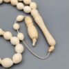 High-resolution macro photograph of a 63.47-gram handmade natural camel bone 33-bead Islamic Tasbih (prayer beads) laid out on a neutral studio backdrop, showcasing smooth ivory-hued barley-cut bone beads, carved separators, and a masterfully turned main pillar (imame).