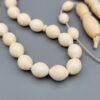 High-resolution macro photograph of a 63.47-gram handmade natural camel bone 33-bead Islamic Tasbih (prayer beads) laid out on a neutral studio backdrop, showcasing smooth ivory-hued barley-cut bone beads, carved separators, and a masterfully turned main pillar (imame).