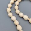 High-resolution macro photograph of a 63.47-gram handmade natural camel bone 33-bead Islamic Tasbih (prayer beads) laid out on a neutral studio backdrop, showcasing smooth ivory-hued barley-cut bone beads, carved separators, and a masterfully turned main pillar (imame).