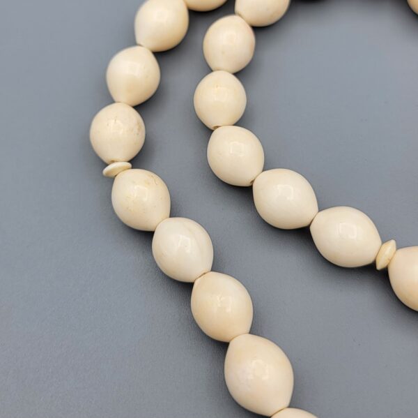 High-resolution macro photograph of a 63.47-gram handmade natural camel bone 33-bead Islamic Tasbih (prayer beads) laid out on a neutral studio backdrop, showcasing smooth ivory-hued barley-cut bone beads, carved separators, and a masterfully turned main pillar (imame).
