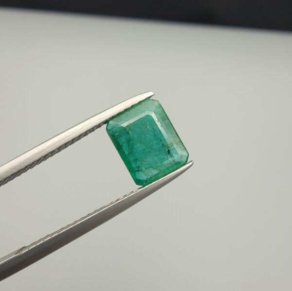 Multi-angle macro photographs of a 1.86-carat natural Zambian emerald (Zamrud) held in metal tweezers, showcasing a classic step-cut emerald octagonal shape, vibrant leafy green hue, and characteristic natural internal inclusions (jardin) across the table.