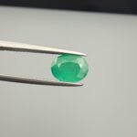 Macro photograph of a 1.79-carat natural Zambian emerald (Zamrud) held in metal tweezers, showcasing a faceted oval cut, vivid green saturation, and fine natural internal inclusions (jardin) across the table.