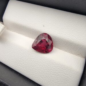 High-resolution macro photograph of a 3.13-carat natural Madagascar Rhodolite Garnet gemstone set against a white textured leather display bed, showcasing a masterfully faceted pear cut with rich, saturated raspberry-red hues and vivid purplish-pink brilliance.