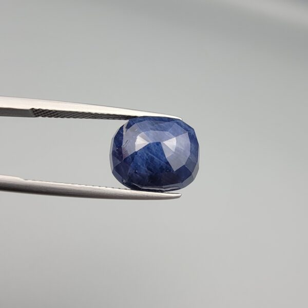 Multi-angle macro photographs of a massive 10.33-carat natural unheated Afghan blue indigo sapphire (Neelam) held in gem tweezers, showcasing a faceted oval cut, deep rich indigo blue hue, and silk inclusion pattern.