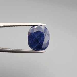 Multi-angle macro photographs of a massive 10.33-carat natural unheated Afghan blue indigo sapphire (Neelam) held in gem tweezers, showcasing a faceted oval cut, deep rich indigo blue hue, and silk inclusion pattern.