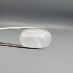 Multi-angle macro photographs showing a massive 41.67-carat natural Durr-e-Najaf (Clear Rock Crystal Quartz) cabochon held in metal tweezers and displayed on fingertips, showcasing an elongated smooth oval dome, water-clear transparency, and subtle organic internal veil growth.