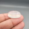 Multi-angle macro photographs showing a massive 41.67-carat natural Durr-e-Najaf (Clear Rock Crystal Quartz) cabochon held in metal tweezers and displayed on fingertips, showcasing an elongated smooth oval dome, water-clear transparency, and subtle organic internal veil growth.