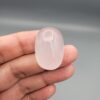 Macro photograph showing a monumental 75.44-carat natural Durr-e-Najaf (Clear Rock Crystal Quartz) cabochon resting on fingertips, featuring a large smooth oval dome, water-clear transparency, and subtle organic internal veil inclusions.